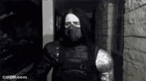 A Black And White Photo Of A Man In A Mask Standing In Front Of A Brick Wall . GIF