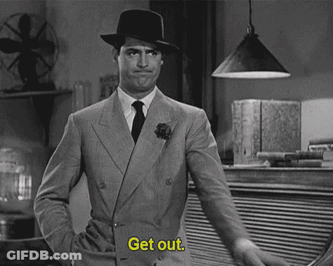 A Black And White Photo Of A Man In A Suit And Hat Pointing At Something . GIF