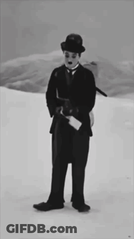 A Black And White Photo Of A Man In A Suit And Hat Standing In The Snow GIF