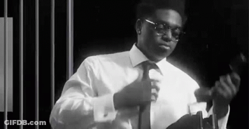A Black And White Photo Of A Man In A Suit And Tie Adjusting His Tie . GIF