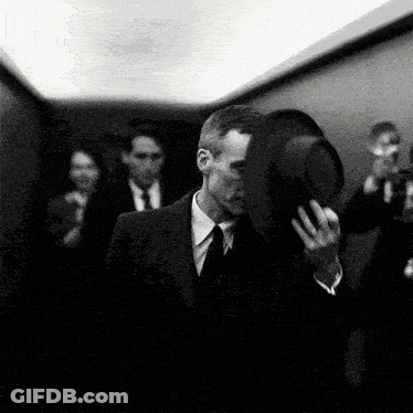 A Black And White Photo Of A Man In A Suit And Tie Holding A Hat GIF