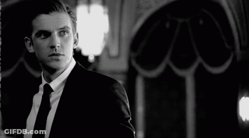 A Black And White Photo Of A Man In A Suit And Tie Looking At Himself In A Mirror . GIF