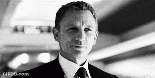 A Black And White Photo Of A Man In A Suit And Tie Looking At The Camera . GIF