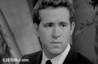 A Black And White Photo Of A Man In A Suit And Tie Making A Face . GIF