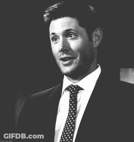 A Black And White Photo Of A Man In A Suit And Tie Smiling GIF