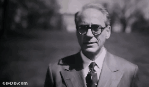 A Black And White Photo Of A Man In A Suit And Tie Standing In A Park . GIF