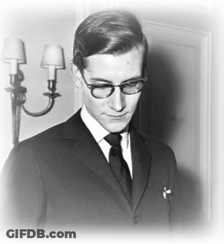 A Black And White Photo Of A Man In A Suit And Tie With Glasses GIF