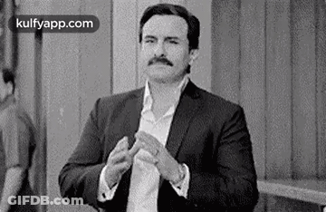 A Black And White Photo Of A Man In A Suit Clapping His Hands . GIF