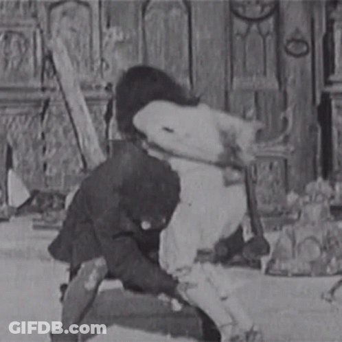 A Black And White Photo Of A Man In A Suit Holding A Woman 'S Leg . GIF