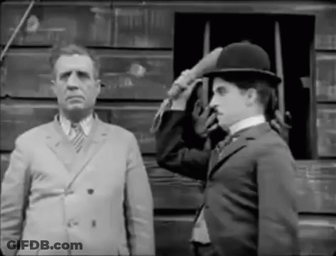 A Black And White Photo Of A Man In A Suit Saluting Another Man In A Hat . GIF