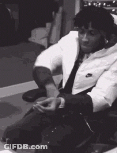 A Black And White Photo Of A Man In A Suit Sitting In A Chair . GIF