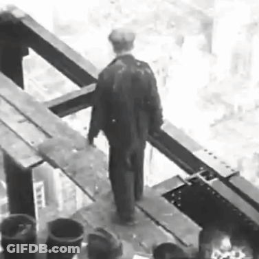 A Black And White Photo Of A Man In A Suit Standing On A Bridge . GIF