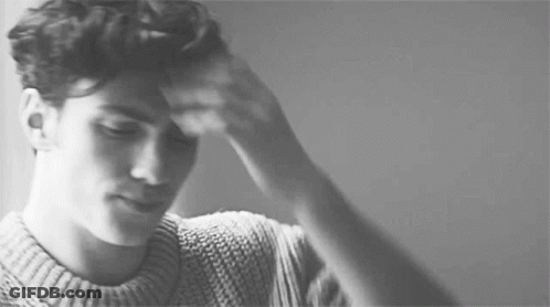 A Black And White Photo Of A Man In A Sweater Holding His Head . GIF
