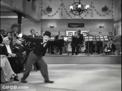 A Black And White Photo Of A Man In A Top Hat Dancing In Front Of An Orchestra GIF