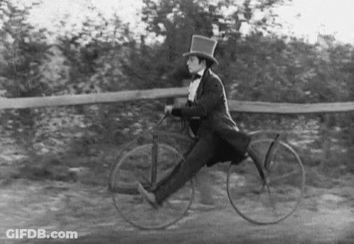 A Black And White Photo Of A Man In A Top Hat Riding A Bike . GIF