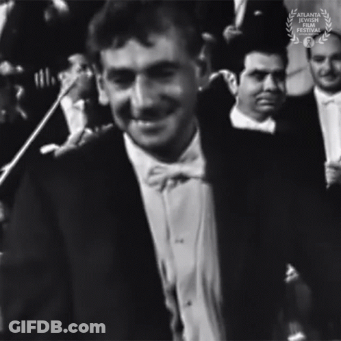 A Black And White Photo Of A Man In A Tuxedo And Bow Tie With A Laurel Wreath In The Corner GIF