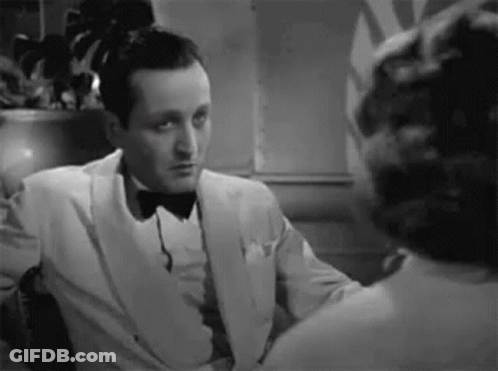 A Black And White Photo Of A Man In A Tuxedo Talking To A Woman . GIF