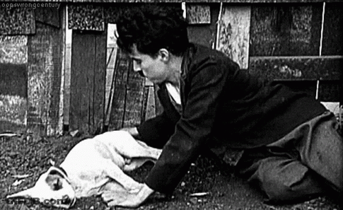A Black And White Photo Of A Man Kneeling Down With A Dog . GIF