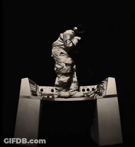A Black And White Photo Of A Man Kneeling On A Desk With A Few Buttons On It Including One That Says 100 GIF