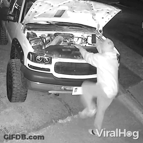 A Black And White Photo Of A Man Looking Under The Hood Of A White Truck GIF