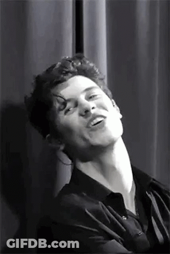 A Black And White Photo Of A Man Making A Funny Face While Standing In Front Of A Curtain . GIF