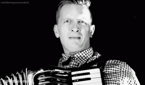 A Black And White Photo Of A Man Playing An Accordion GIF