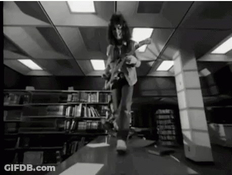 A Black And White Photo Of A Man Playing An Electric Guitar In A Library . GIF