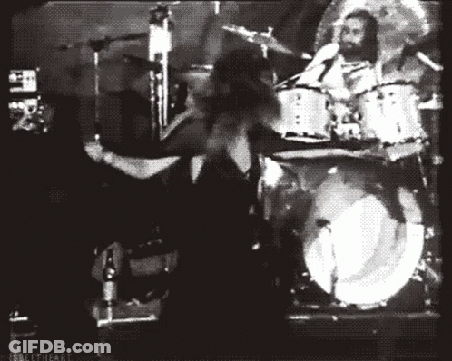 A Black And White Photo Of A Man Playing Drums In Front Of A Drum Set GIF
