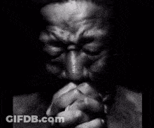 A Black And White Photo Of A Man Praying With His Hands Folded In Front Of His Face . GIF