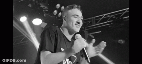 A Black And White Photo Of A Man Singing Into A Microphone On Stage . GIF