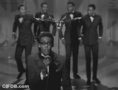 A Black And White Photo Of A Man Singing Into A Microphone While A Group Of Men Play Instruments . GIF