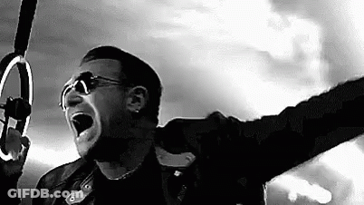 A Black And White Photo Of A Man Singing Into A Microphone While Holding A Ring . GIF