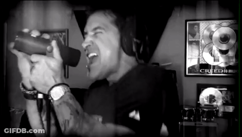 A Black And White Photo Of A Man Singing Into A Microphone With A Creed Poster Behind Him GIF