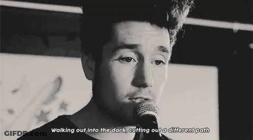 A Black And White Photo Of A Man Singing Into A Microphone With The Words Walking Out Into The Dark Cutting Out A Differ GIF