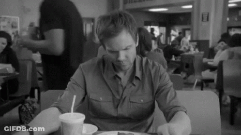 A Black And White Photo Of A Man Sitting At A Table With A Plate Of Food GIF