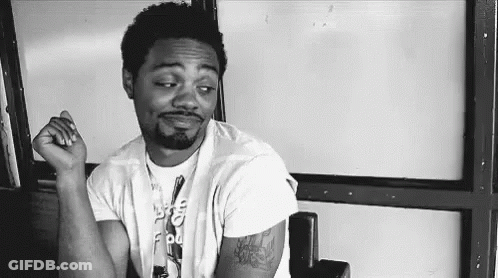 A Black And White Photo Of A Man Sitting In A Chair With His Hand On His Chin . GIF