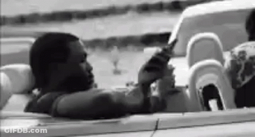A Black And White Photo Of A Man Sitting In A Convertible . GIF