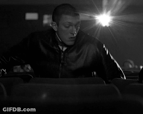 A Black And White Photo Of A Man Sitting In A Theater GIF