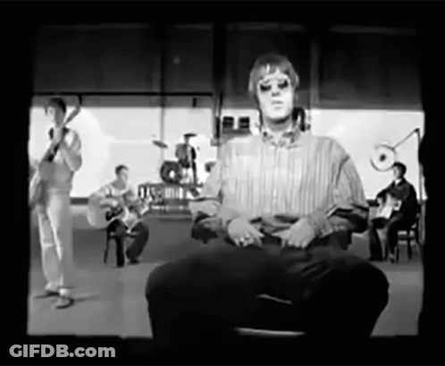 A Black And White Photo Of A Man Sitting In Front Of A Band GIF