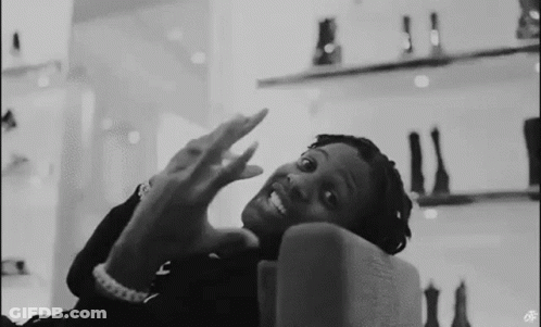 A Black And White Photo Of A Man Sitting On A Couch With His Hands Up . GIF