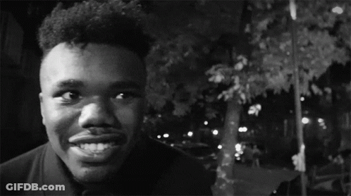 A Black And White Photo Of A Man Smiling With A Car In The Background GIF
