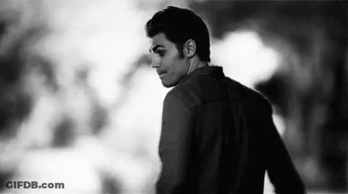 A Black And White Photo Of A Man Standing In A Dark Room Looking Over His Shoulder . GIF