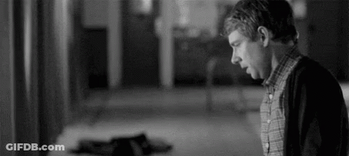 A Black And White Photo Of A Man Standing In A Hallway Looking Down . GIF
