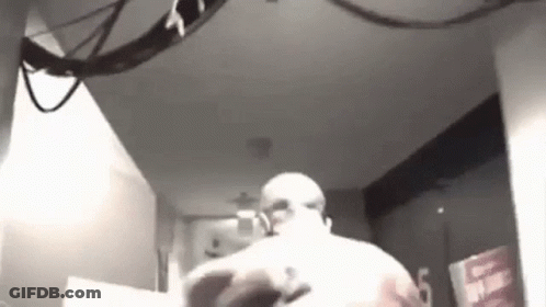 A Black And White Photo Of A Man Standing In A Room With A Ceiling Fan . GIF