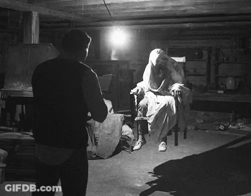 A Black And White Photo Of A Man Standing In Front Of A Ghost In A Chair GIF