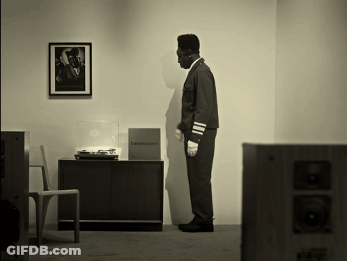 A Black And White Photo Of A Man Standing In Front Of A Record Player With A Box That Says B&w National On It GIF