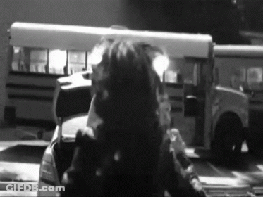 A Black And White Photo Of A Man Standing In Front Of A School Bus GIF