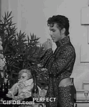 A Black And White Photo Of A Man Standing In Front Of A Table With A Bottle Of Wine And A Statue . GIF