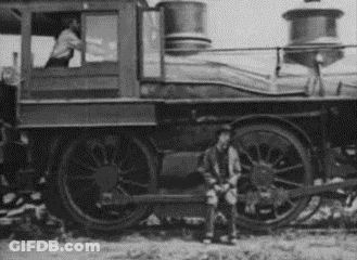 A Black And White Photo Of A Man Standing In Front Of A Train . GIF
