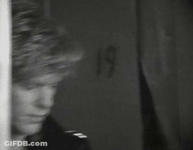 A Black And White Photo Of A Man Standing In Front Of A Wall . GIF